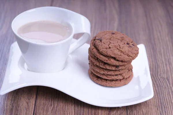 tasty chocolate biscuits with cup of latte on white wavy saucer