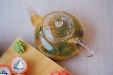 Suşi, somon, avokado ve yeşil çaydanlık ile ahşap bir masada. 