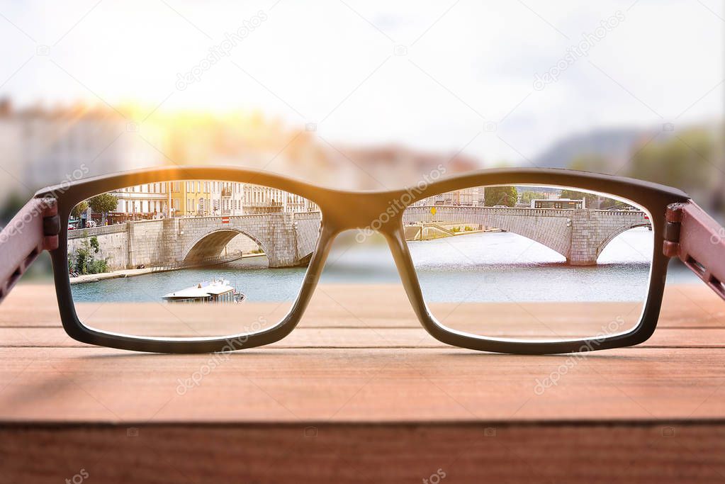 Concept of eyesight correction with glasses on a bridge handrails focusing on a cityscape. Front view. Horizontal composition