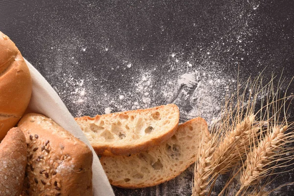 Bread on basket with cloth and black wooden table with wheat and flour close up. Top view. Horizontal composition