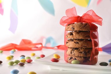 Çikolata kurabiye plaka üzerinde renk bantları arka plan ile çanak üzerinde kırmızı yay ile yığını. Parti kavramı. Önden görünüm. Yatay kompozisyon