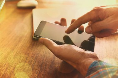 Ellerini bir adamın altın güneş ışını ile kahverengi ahşap bir masa üzerinde bir telefon dokunmak. Yatay kompozisyon.