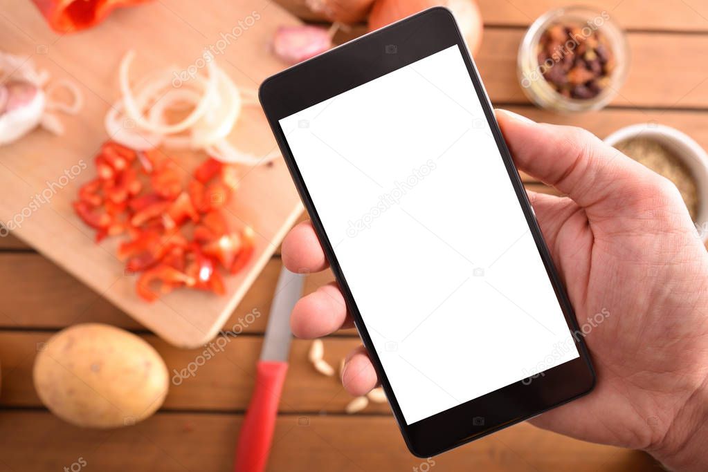 Hand with mobile in kitchen preparing a menu. Concept of recipes in digital book. Horizontal composition. Top view