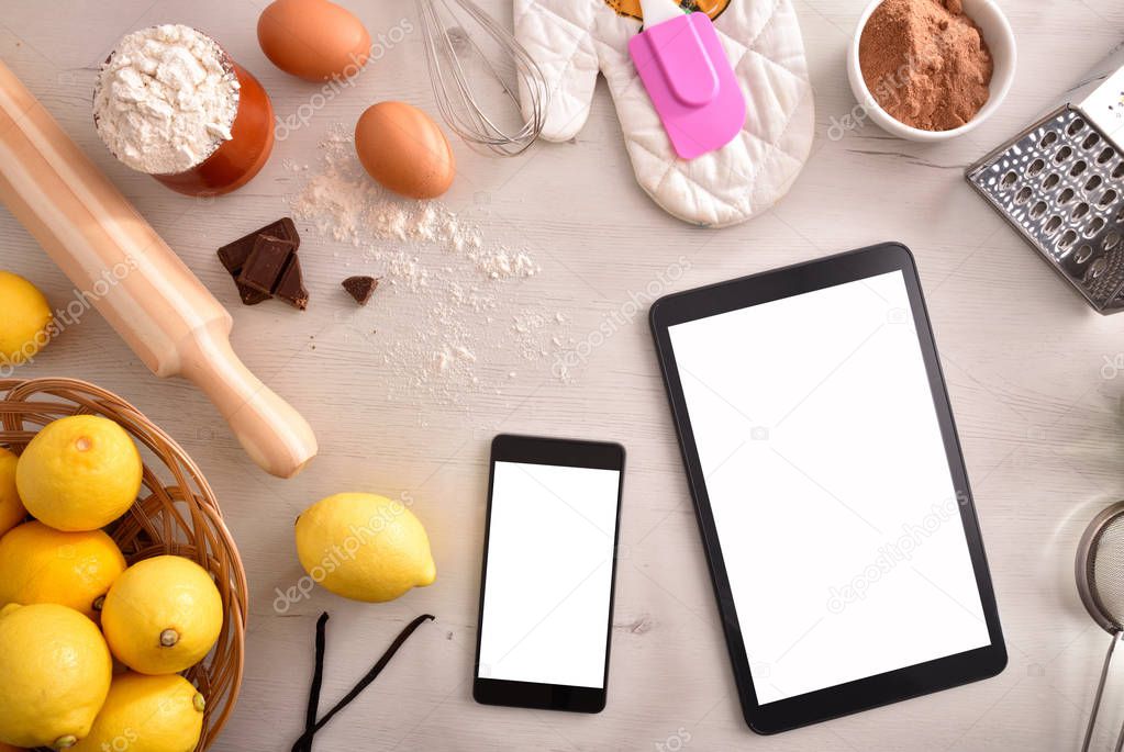 Pastry ingredients on a white wooden table and mobile devices. Concept of recipes in digital book. Horizontal composition. Top view