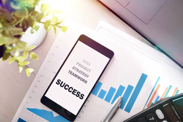 Message on a mobile about the development of a strategic plan of success at work with graphics on a desk in the background