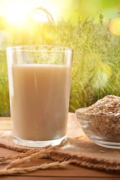 Oat drink in glass and cereal flakes on wood table in nature. Vertical composition. Front view