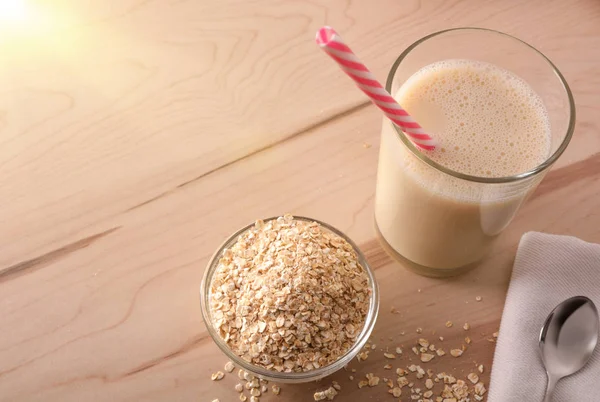 Oat drink in glass and cereal flakes on kitchen bench with white background. Horizontal composition. Top view