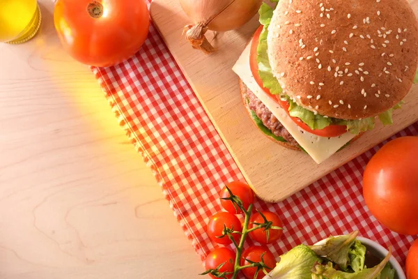 Homemade beef burger with ingredients on wood table with checkered tablecloth in kitchen. Top view. Horizontal composition.