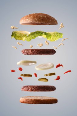 Marul soğan ve turşu gri degrade izole arka plan üzerinde yerlerinde kırık aşağı malzemelerle yüzer kişilik hamburger. Önden görünüm. Dikey kompozisyon.