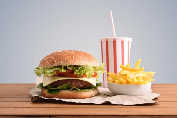 Beef burger,chips and soda on wooden table with golden backgorund. Front view. Horizontal composition.