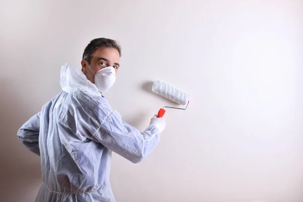 Background with professional painter with working overalls and roller on the back of a white wall looking down his back. Concept of painter and paint supplies. Horizontal composition.