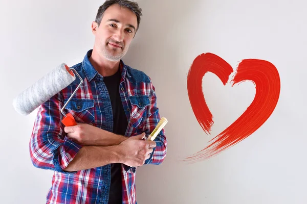 Man with painting tools on hands and heart painted on the wall. Concept of love for decoration of interior painting. Front view. Horizontal composition.