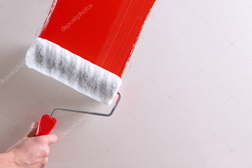 Man's hand painting a red sample with roller on a white wall. Horizontal composition.