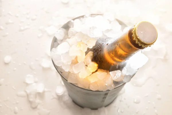 Beer bottle in metal bucket full of ice cubes on white table — Stock Photo, Image