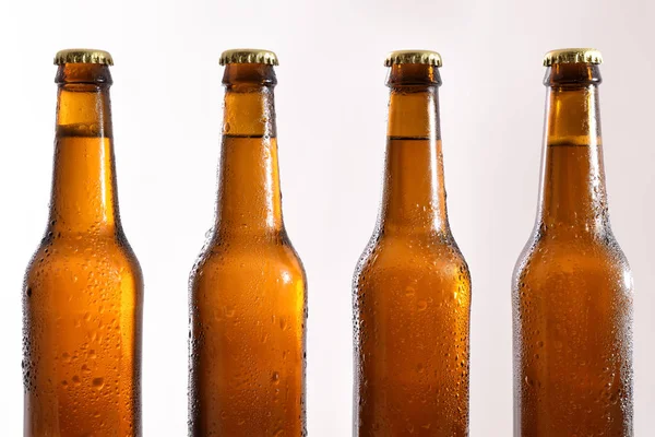 Row of four closed glass bottles with fresh beer on white backgr — Stock Photo, Image