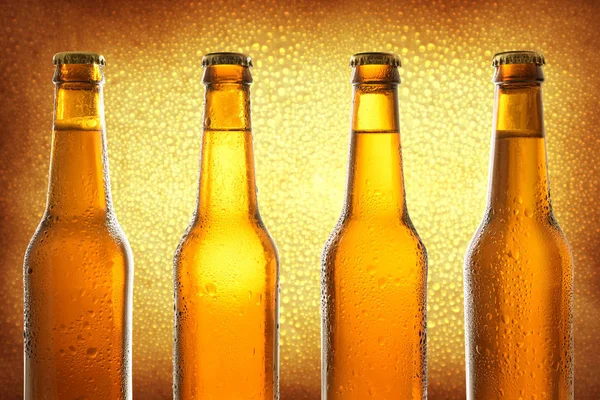 Row of four closed glass bottles with fresh beer on golden backg — Stock Photo, Image