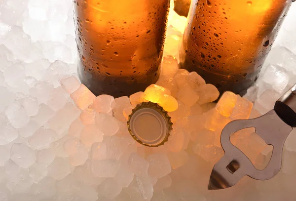 Beer glass bottles on ice with cap and bottle opener — Stock Photo, Image