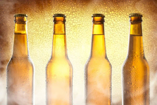 Row glass bottles with beer with golden background and steam