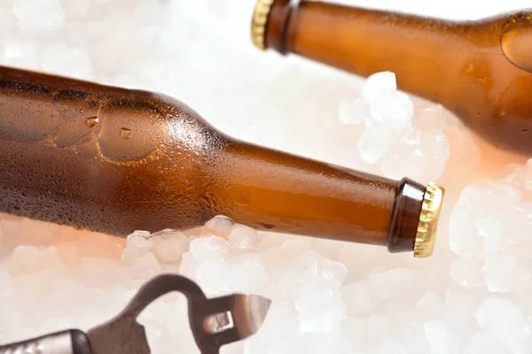 Duas garrafas de cerveja deitadas em gelo picado com abridor de garrafas — Fotografia de Stock