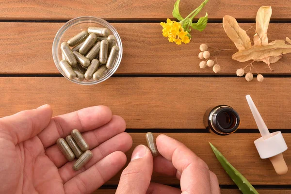 Hands taking natural medicine capsules on wooden table with plan