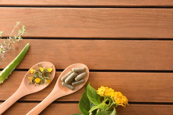 Natural medicine capsules on and plants on wood spoon top