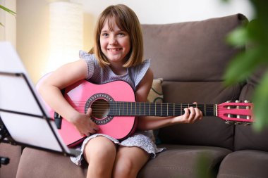 Oturma odasındaki kanepede oturup gitar çalışmasına gülen kız.