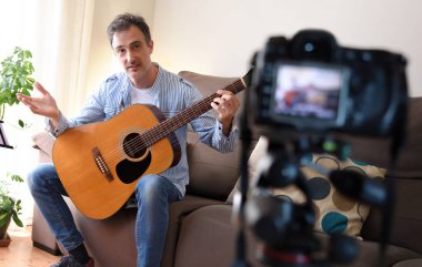 Video blogcusu oturma odasında kamera kaydı olan bir gitarı inceliyor.