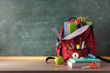 Okul malzemeleriyle dolu sırt çantası ahşap masa ve ön görüş için boş alanı olan yeşil karatahta