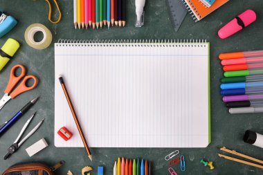 Yeşil karatahtanın etrafında çizgiler ve okul malzemeleri olan bir defter aç