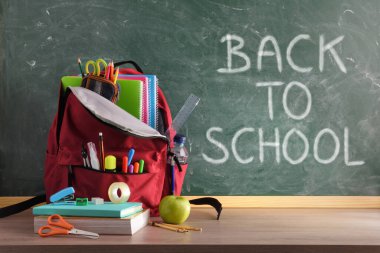 Okul malzemeleriyle dolu sırt çantası ahşap masa ve ön görüş için boş alanı olan yeşil karatahta