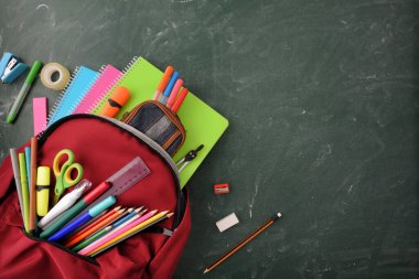 Okul malzemeleriyle dolu sırt çantası yeşil tahtanın üzerinde. Üst görünümü yazmak için boş bir alan var.