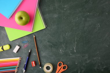 Not defterleri, renkli kalemler ve yeşil karatahtadaki diğerleri gibi okul eğitim malzemeleri. Üst görünüm.