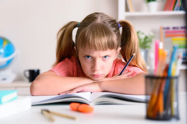 Little girl studying at home angry with crossed arms over book at study desk at home