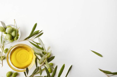 Beyaz masada izole edilmiş zeytin yağı ve zeytin dallarıyla dolu cam bir kase. Üst görünüm.