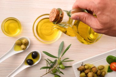 Yemek için farklı zeytin çeşitleri ve ahşap mutfak tezgahı ve cam kase üzerindeki kaplarda yağ. Üst görünüm.