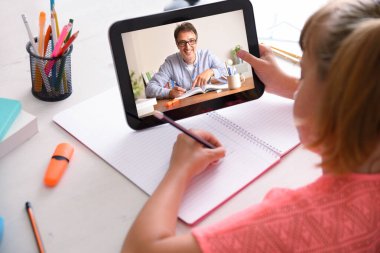 Uzaklık öğretmeni olan çevrimiçi öğrenci evde tabletle ders alıyor. Arka yükseltilmiş görünüm.
