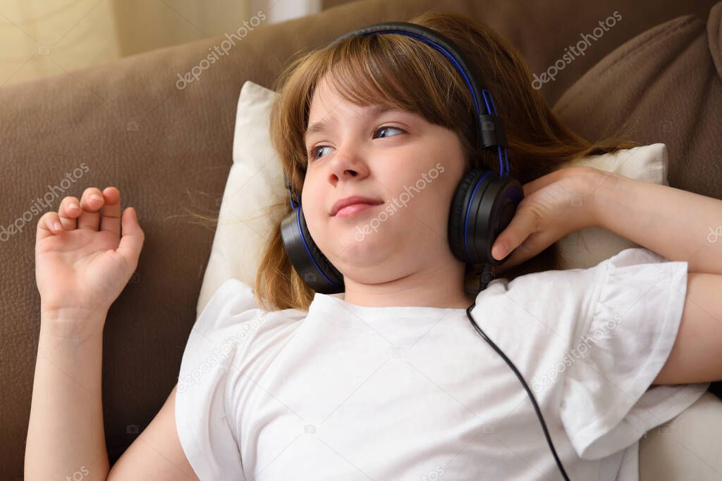 Girl with helmets listening to music lying on the sofa at home in a quiet and warm environment. Top view.