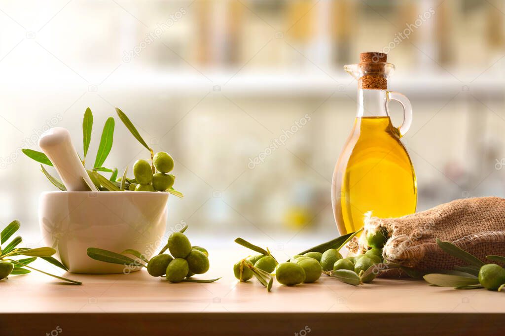 Preparation of olive oil seed in ceramic glass for body and culinary care on table with mortar and sack of olives. Front view.