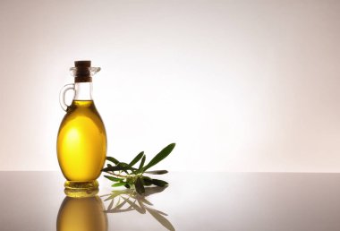 Cam sehpada zeytinyağı dolu cam kap ve gri gradyan izole arkaplan. Metin için boşluk olan sol taraftaki kompozisyon.