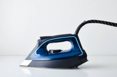 Mavi buhar ütüsünün yan görüntüsü beyaz masaya ve beyaz izole arka plana yansıyor. Ön görünüm.