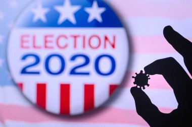 Hand silhouette hold covid 19 virus. Logo of USA presidental Election 2020 in background. US presidential elections are threatened by coronavirus and may be postponed clipart