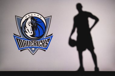 NEW YORK, USA, JUN 18, 2020: Dallas Mavericks logo of professional basketball club in american league. Silhouette of basket player in foreground. Sport concept photo, edit space. clipart