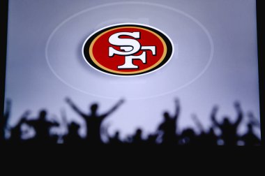 San Francisco 49 'lular. Taraftarlar Amerikan Ulusal Foorbol Ligi 'nin profesyonel takımını destekliyor. Taraftarların silueti ön planda. Büyük ekranda logo.