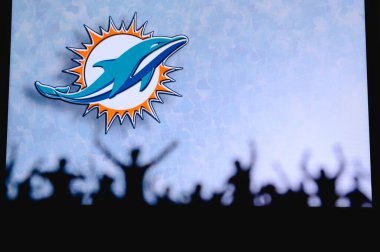 Miami Dolphins. Fans support professional team of American National Foorball League. Silhouette of supporters in foreground. Logo on the big screen. clipart