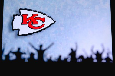 Kansas City Chiefs. Fans support professional team of American National Foorball League. Silhouette of supporters in foreground. Logo on the big screen. clipart