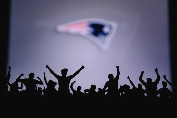 ニューイングランドの愛国者 ファンはアメリカン ナショナル フットボール リーグのプロチームをサポートしている 前景の支持者のシルエット 大きな画面上のロゴ — ストック写真