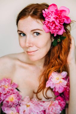 Çilli, pembe şakayık çiçekli, çıplak omuzlu bir elbise giymiş kızıl saçlı kız. Doğal güzellik. Kendini sevme ve görünüm kavramı..