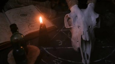 Boynuzlu beyaz keçi kafatası, açık eski kitap, rünler, cadı masasında siyah mumlar. Esrarengiz, esrarengiz, kehanet ve cadı kavramı. Cadılar Bayramı, Ölü Kavram Günü.