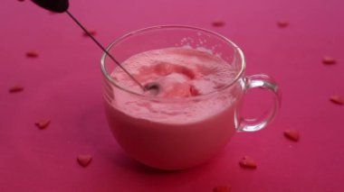 Pembe arka planda büyük cam bir fincanda pembe ay sütü yapmak için köpüklü süt kullanmak.