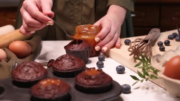 女性の手はチョコレートカップケーキにキャラメル充填を注ぎます 女性は台所でおいしいカップケーキを準備します ビデオは自家製マフィンを作る完全なプロセスを示しています — ストック動画